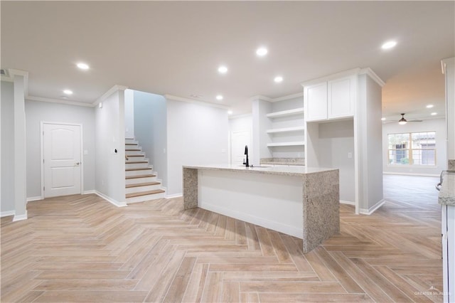 interior space featuring white cabinets, ceiling fan, ornamental molding, light stone counters, and light parquet flooring