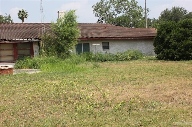 rear view of property featuring stucco siding, a chimney, a tiled roof, and a yard