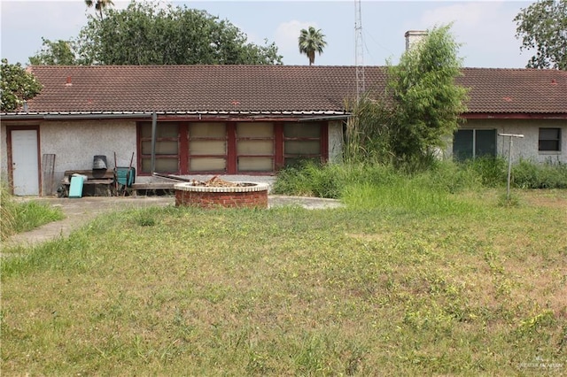 back of house featuring stucco siding, a yard, and a tile roof
