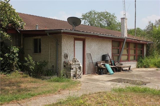 rear view of house featuring a patio, a chimney, stucco siding, and a tiled roof