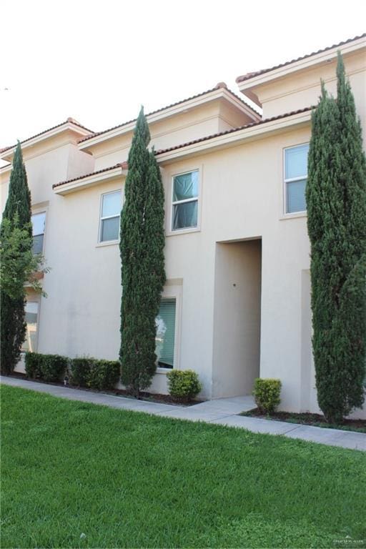 exterior space with a tiled roof, a front lawn, and stucco siding