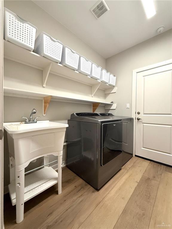 laundry area featuring sink, light wood-type flooring, and washing machine and clothes dryer