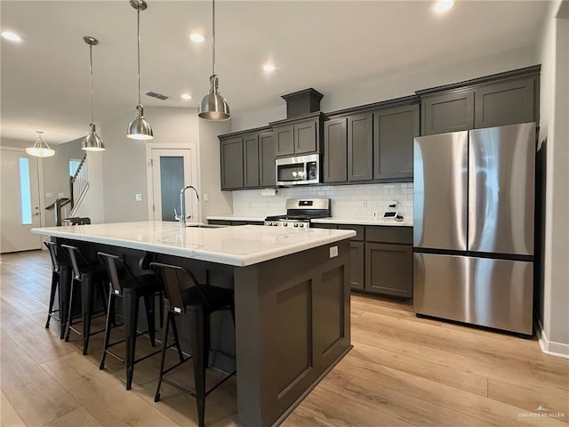 kitchen featuring sink, a large island with sink, stainless steel appliances, and hanging light fixtures