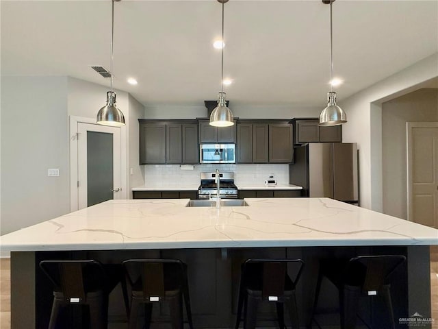 kitchen with a large island with sink, decorative backsplash, pendant lighting, and appliances with stainless steel finishes