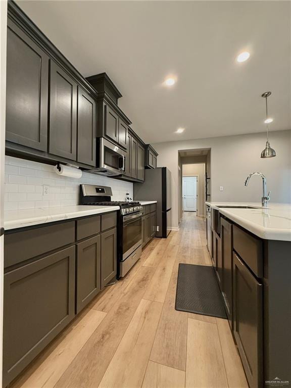 kitchen with decorative backsplash, stainless steel appliances, sink, pendant lighting, and light hardwood / wood-style flooring