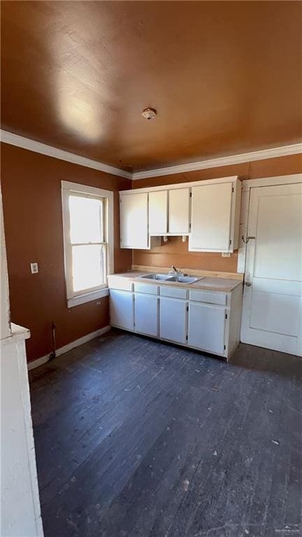 kitchen featuring a sink, white cabinets, crown molding, light countertops, and dark wood-style flooring