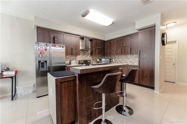 kitchen with light tile patterned floors, stainless steel appliances, a breakfast bar, wall chimney range hood, and decorative backsplash