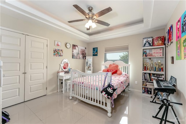 tiled bedroom with a tray ceiling, a closet, a ceiling fan, and baseboards