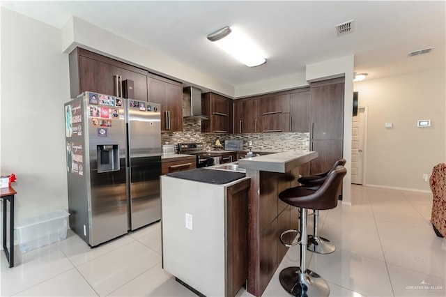 kitchen with stainless steel appliances, a breakfast bar, visible vents, decorative backsplash, and wall chimney exhaust hood