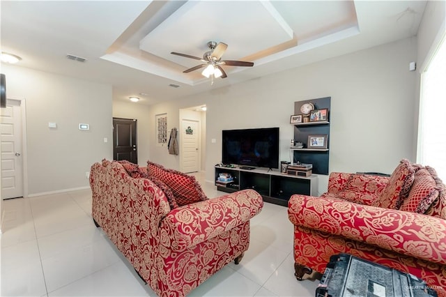 living area with a ceiling fan, a tray ceiling, visible vents, and light tile patterned flooring