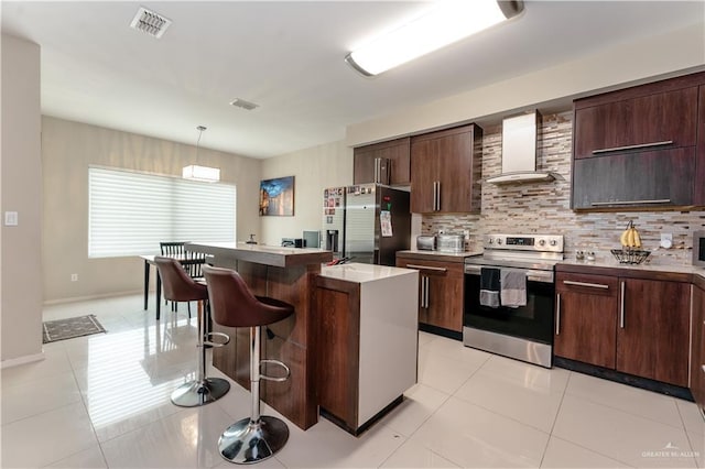 kitchen with a breakfast bar area, backsplash, appliances with stainless steel finishes, light tile patterned flooring, and wall chimney range hood