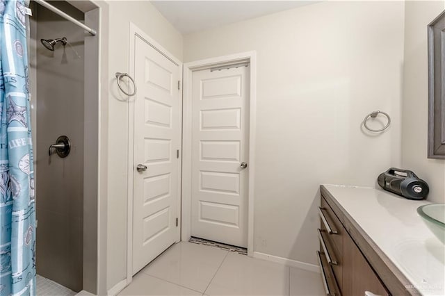 bathroom featuring tile patterned flooring, tiled shower, vanity, and baseboards