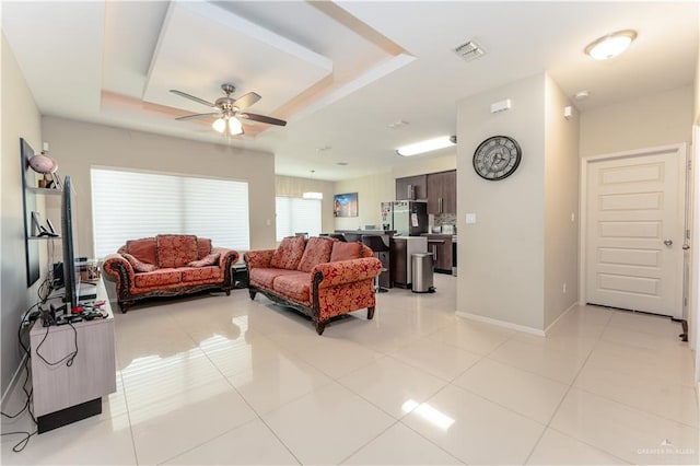 living area featuring light tile patterned flooring, visible vents, baseboards, a ceiling fan, and a tray ceiling