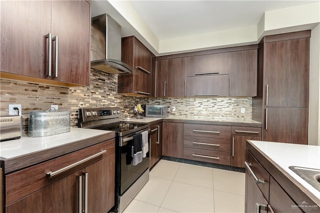 kitchen with wall chimney exhaust hood, backsplash, stainless steel electric range, and light tile patterned floors