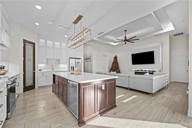 kitchen with a raised ceiling, white cabinets, a kitchen island, and beverage cooler