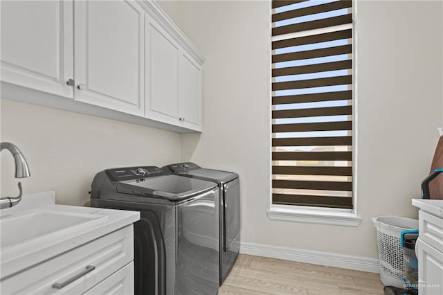 clothes washing area with cabinets, separate washer and dryer, sink, and light hardwood / wood-style flooring