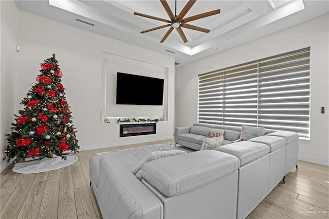 living room with ceiling fan, light wood-type flooring, and a tray ceiling