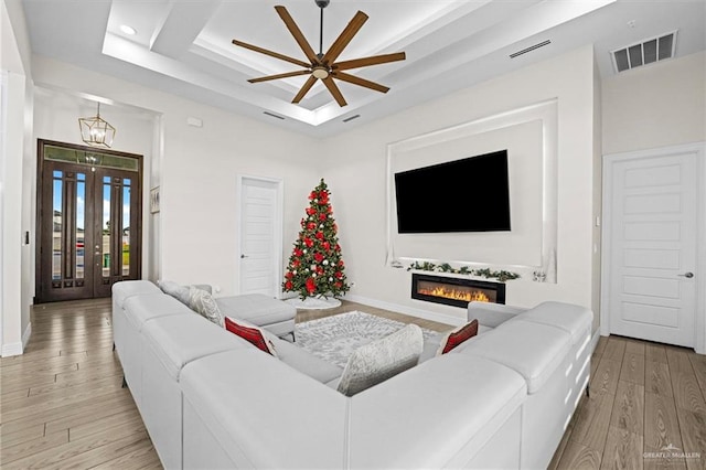 living room with a tray ceiling, ceiling fan with notable chandelier, and light wood-type flooring