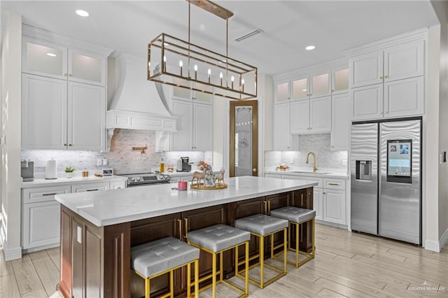 kitchen featuring white cabinetry, a center island, light hardwood / wood-style flooring, custom range hood, and appliances with stainless steel finishes