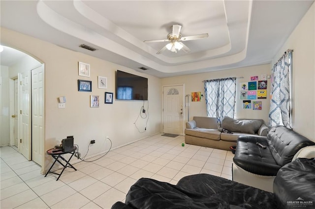 living room with a raised ceiling, ceiling fan, and light tile patterned floors