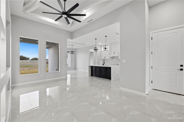 unfurnished living room with a tray ceiling, sink, a high ceiling, and ceiling fan