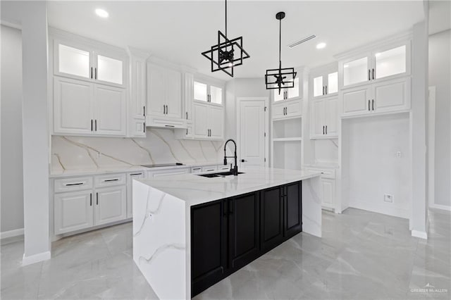 kitchen with a center island with sink, sink, light stone counters, and white cabinetry