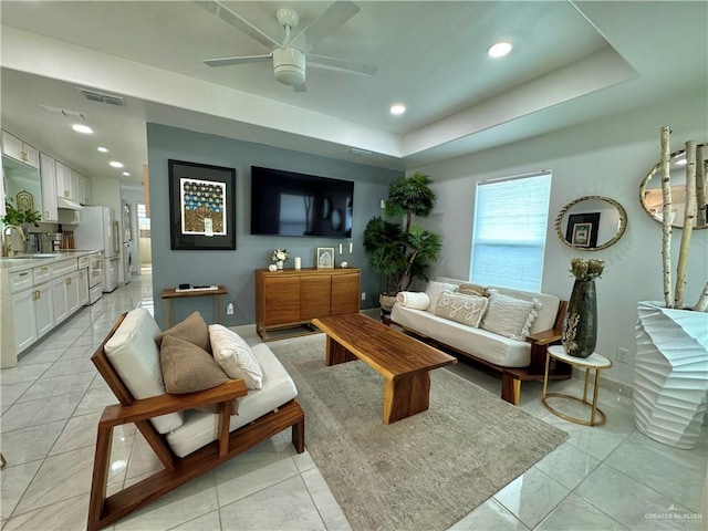 living room featuring a raised ceiling, ceiling fan, and sink