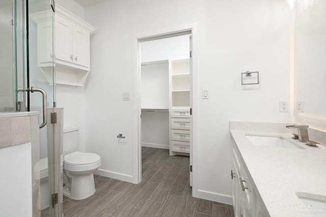 full bath featuring toilet, wood finish floors, vanity, baseboards, and a shower stall