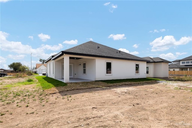 rear view of property featuring roof with shingles, a patio, fence, and stucco siding