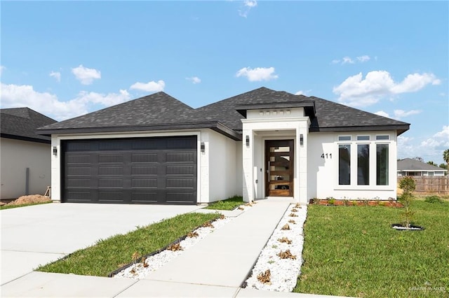 prairie-style home with roof with shingles, stucco siding, a front yard, a garage, and driveway