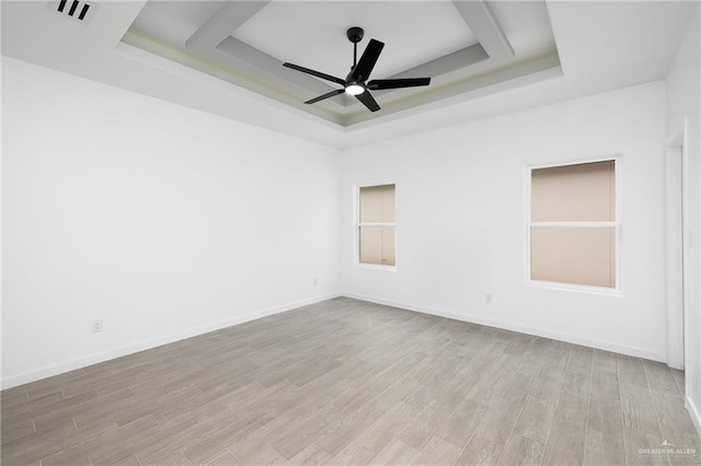 empty room featuring visible vents, baseboards, a raised ceiling, a ceiling fan, and light wood-style flooring