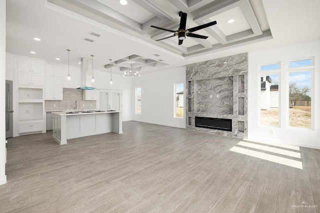 unfurnished living room with light wood-style flooring, a fireplace, coffered ceiling, a ceiling fan, and beam ceiling