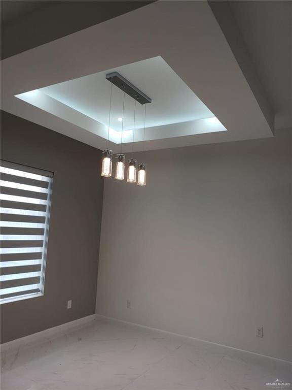 spare room with a raised ceiling, baseboards, and marble finish floor