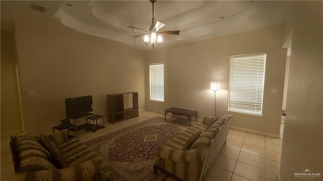 living room with a tray ceiling, ceiling fan, and light tile patterned flooring