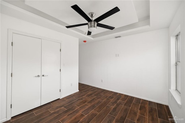 unfurnished bedroom with a raised ceiling, ceiling fan, and a closet