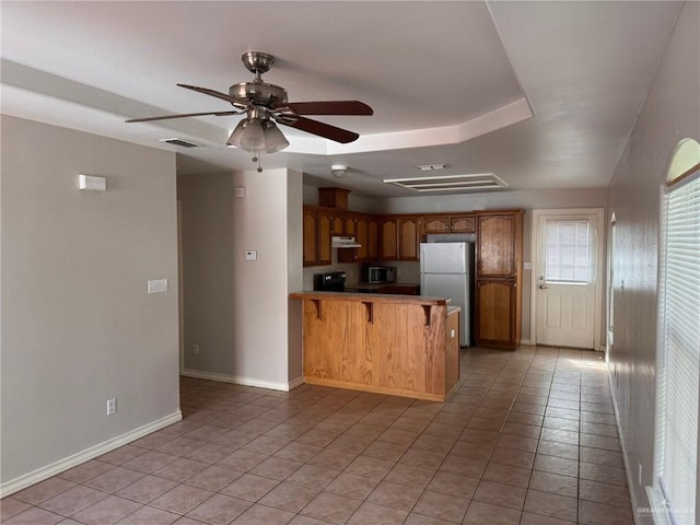 kitchen with a kitchen bar, light tile patterned floors, fridge, kitchen peninsula, and ceiling fan