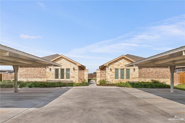 exterior space with covered parking, stone siding, brick siding, and fence