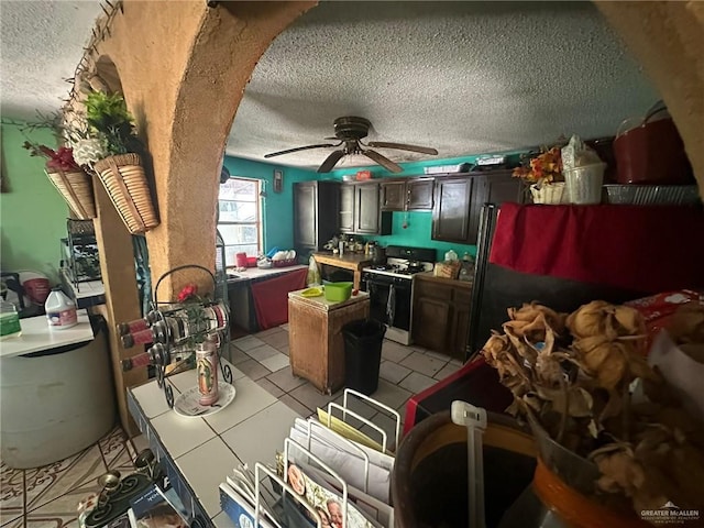 kitchen featuring white gas range, dark brown cabinets, a textured ceiling, ceiling fan, and light tile patterned floors