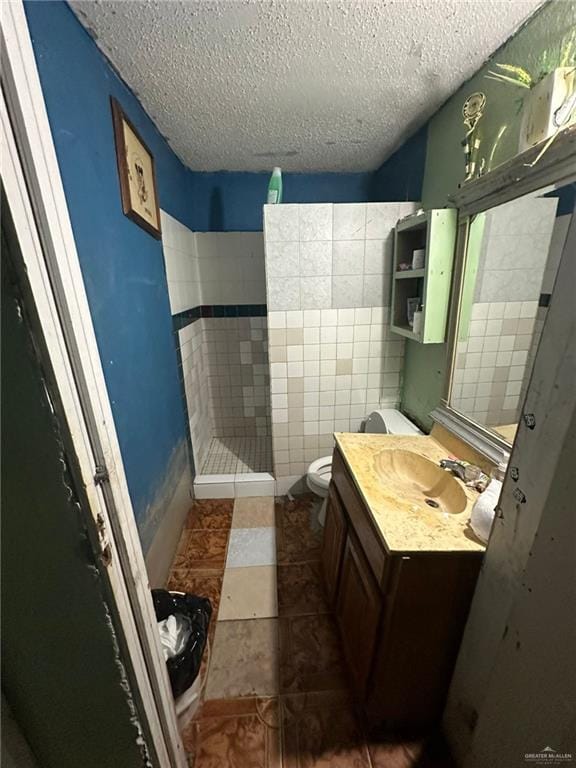 bathroom featuring vanity, tile patterned flooring, toilet, a textured ceiling, and tile walls