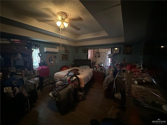 bedroom featuring hardwood / wood-style floors, a tray ceiling, an AC wall unit, and ceiling fan