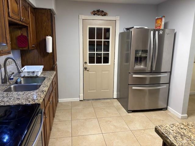 kitchen with sink, stainless steel fridge, light stone countertops, and light tile patterned flooring