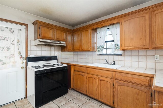 kitchen featuring tile countertops, backsplash, sink, white gas range, and light tile patterned flooring