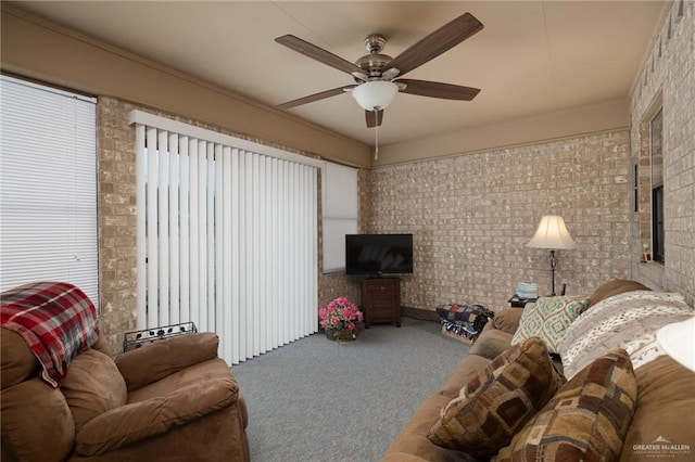 carpeted living room with ceiling fan and brick wall