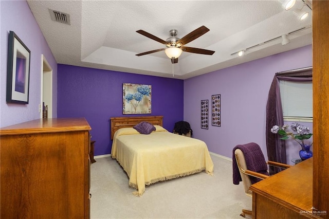 carpeted bedroom featuring a raised ceiling, ceiling fan, track lighting, and a textured ceiling