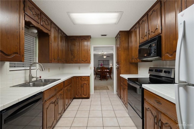 kitchen with light tile patterned flooring, sink, tile countertops, black appliances, and backsplash