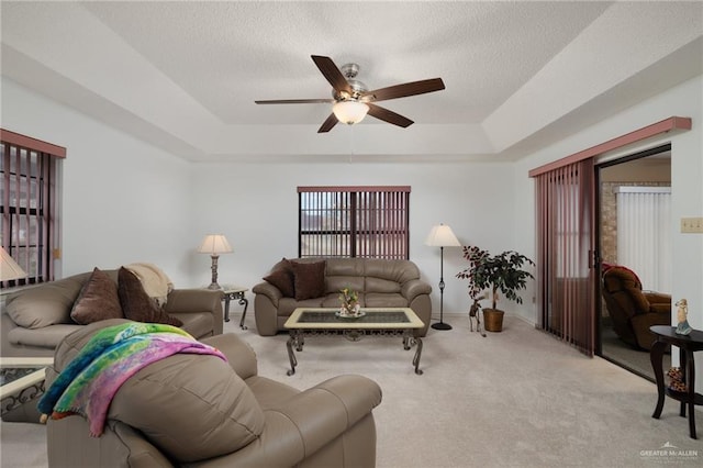 living room featuring a raised ceiling, ceiling fan, light colored carpet, and a textured ceiling