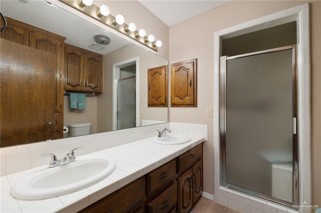 bathroom with vanity, a shower with shower door, a textured ceiling, and toilet