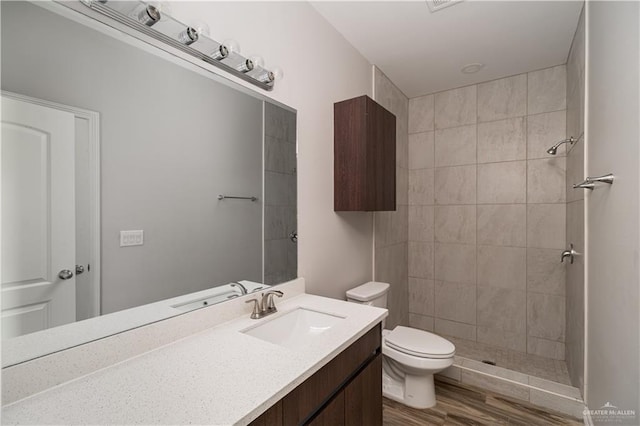 bathroom featuring vanity, wood-type flooring, tiled shower, and toilet