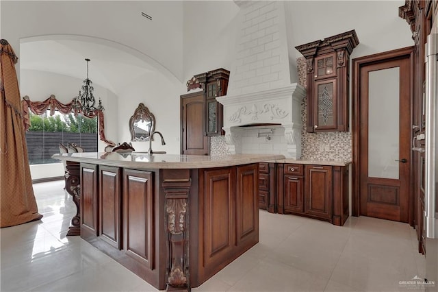 interior space featuring pendant lighting, backsplash, a kitchen island with sink, light tile patterned floors, and a notable chandelier