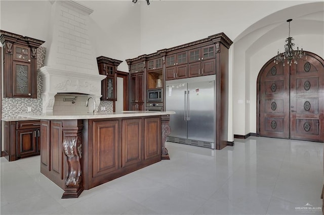 kitchen with built in appliances, a center island with sink, light tile patterned floors, and pendant lighting